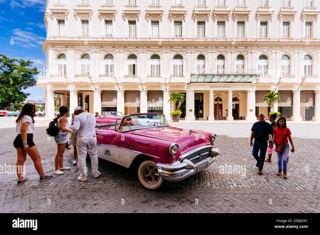 I turisti si trovano vicino a un taxi - almendrón - di fronte al Gran Hotel Manzana Kempinski. L'Avana. Cuba, America Latina e Caraibi Foto Stock