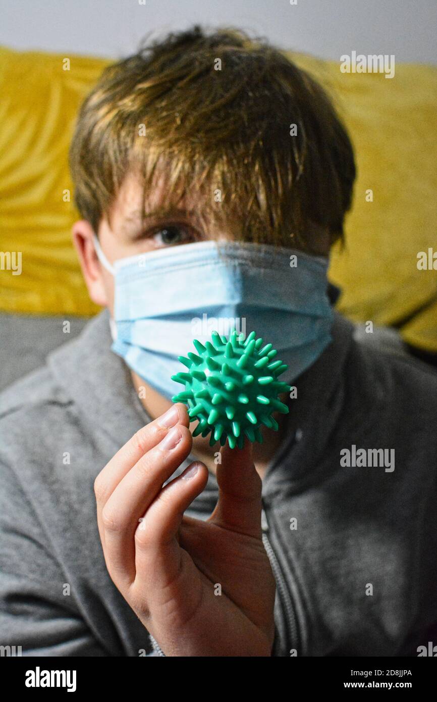 ragazzo adolescente in maschera di faccia che tiene il coronavirus che rappresenta la palla. Foto Stock