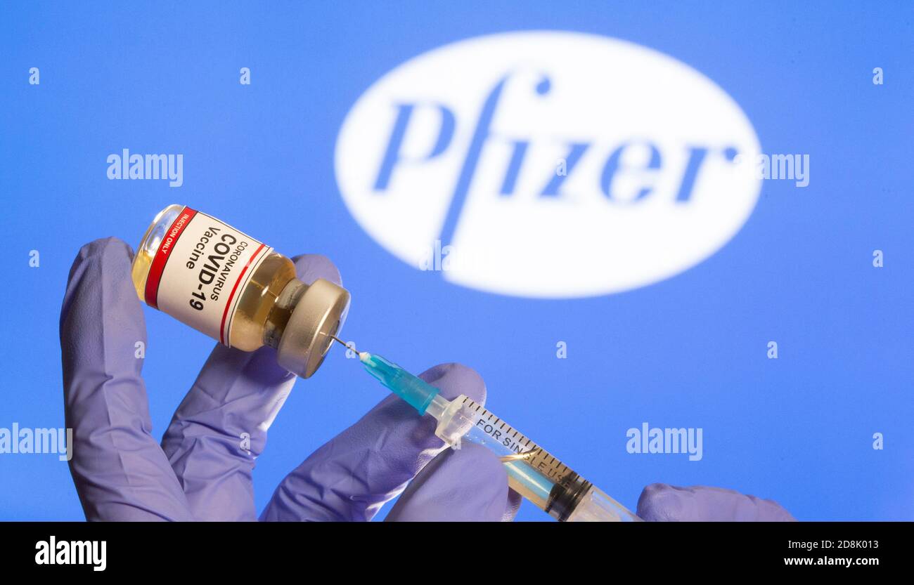 Una donna contiene un piccolo flacone etichettato con un adesivo 'Coronavirus COVID-19 Vaccine' e una siringa medica davanti al logo Pfizer visualizzato in questa illustrazione presa, 30 ottobre 2020. REUTERS/Dado Ruvic Foto Stock
