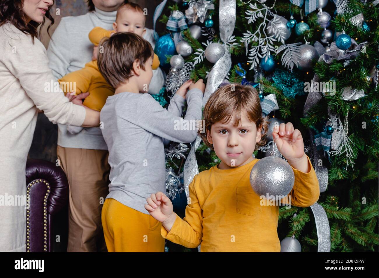 Famiglia felice - padre, mamma e figli tutti insieme decorano l'albero di Natale nel soggiorno. La famiglia con i bambini festeggia le vacanze invernali. Foto Stock