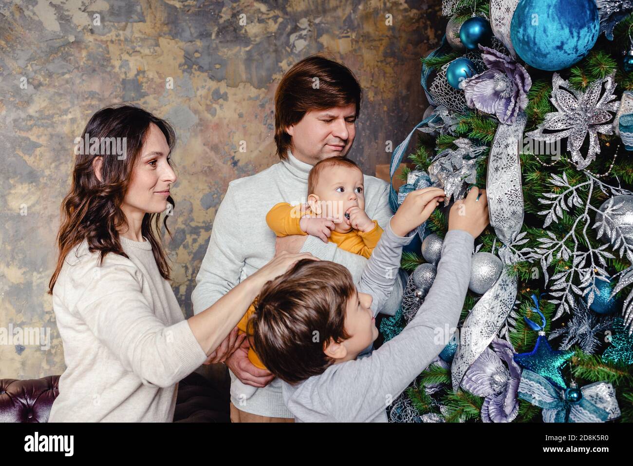 Famiglia felice - padre, mamma e figli tutti insieme decorano l'albero di Natale nel soggiorno. La famiglia con i bambini festeggia le vacanze invernali. Foto Stock