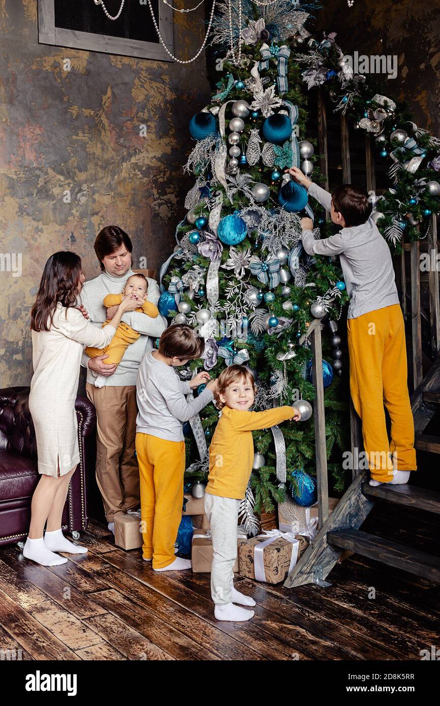 Famiglia felice - padre, mamma e figli tutti insieme decorano l'albero di Natale nel soggiorno. La famiglia con i bambini festeggia le vacanze invernali. Foto Stock
