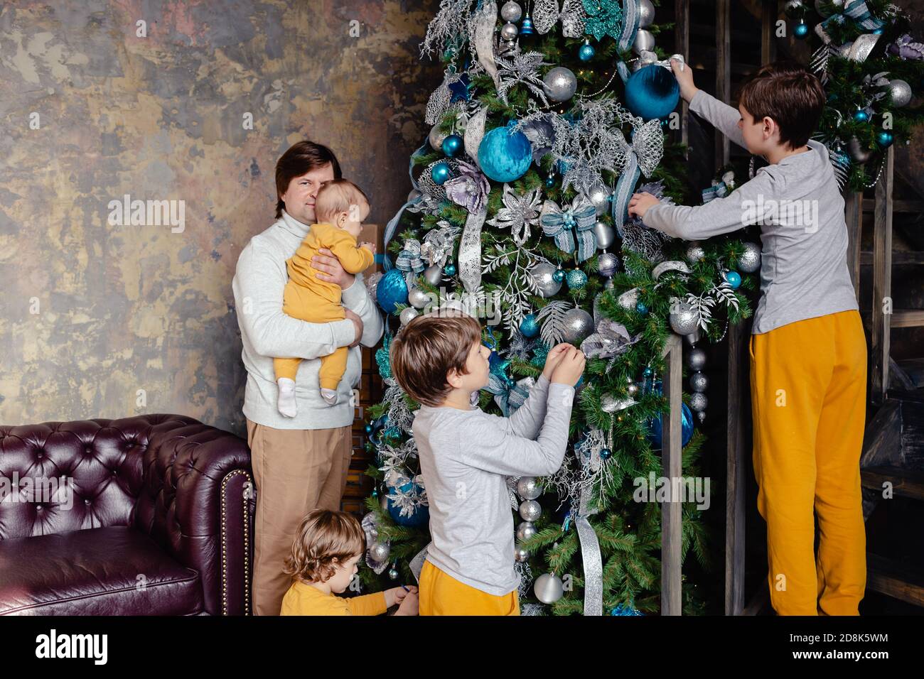 Famiglia felice - padre e figli tutti insieme decorano l'albero di Natale nel soggiorno. La famiglia con i bambini festeggia le vacanze invernali. Foto Stock
