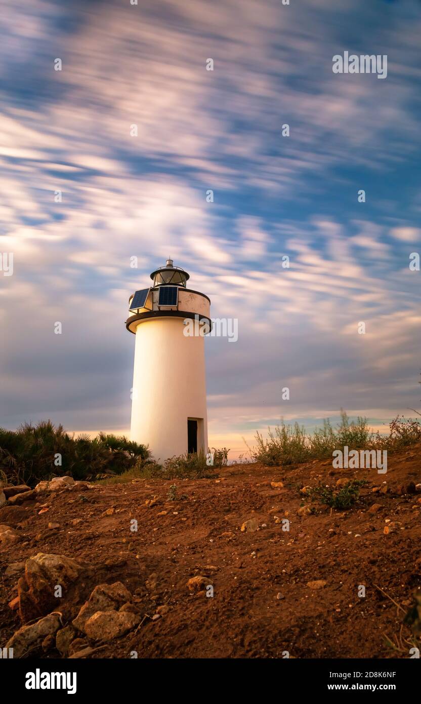 Faro di Porto Conte all'ora d'oro sotto una lunga esposizione cielo nuvoloso Foto Stock