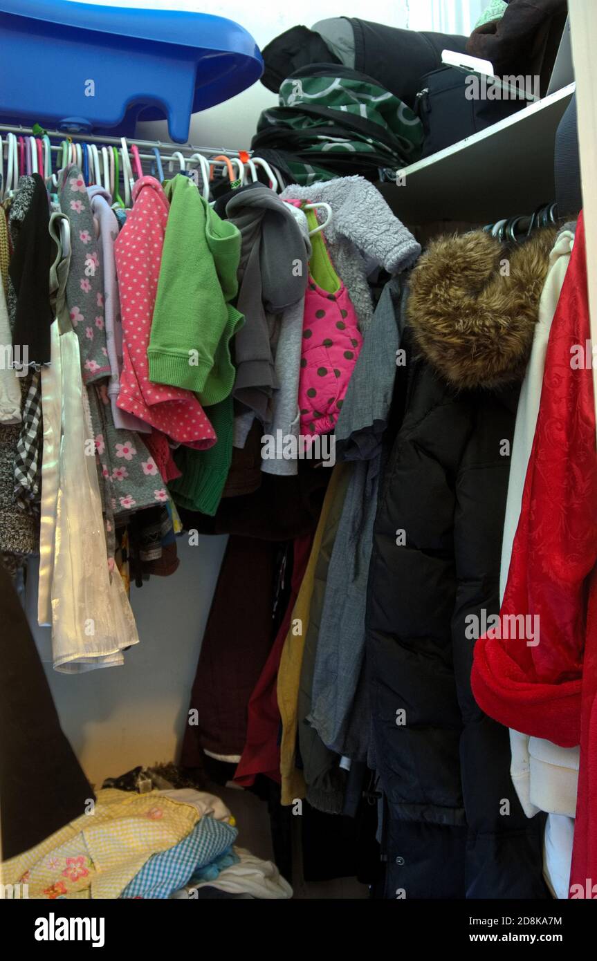 armadio piccolo, stretto con molti vestiti appesi su appendiabiti e cose sugli scaffali Foto Stock