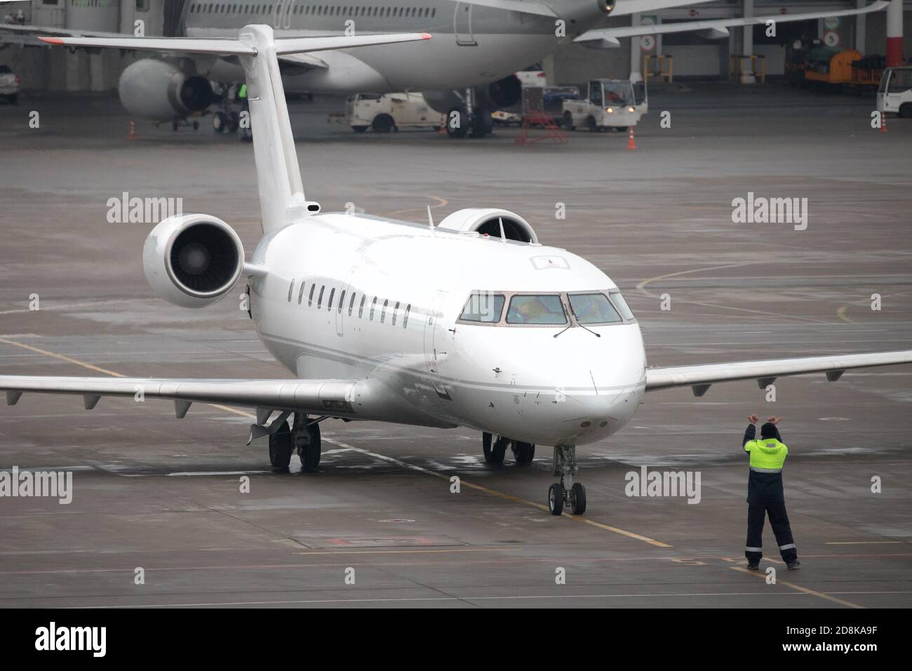 Moderno aereo di linea regionale sul grembiule dell'aeroporto. Il personale di terra del controllore del traffico aeroportuale dà i comandi ad un aereo. Foto Stock