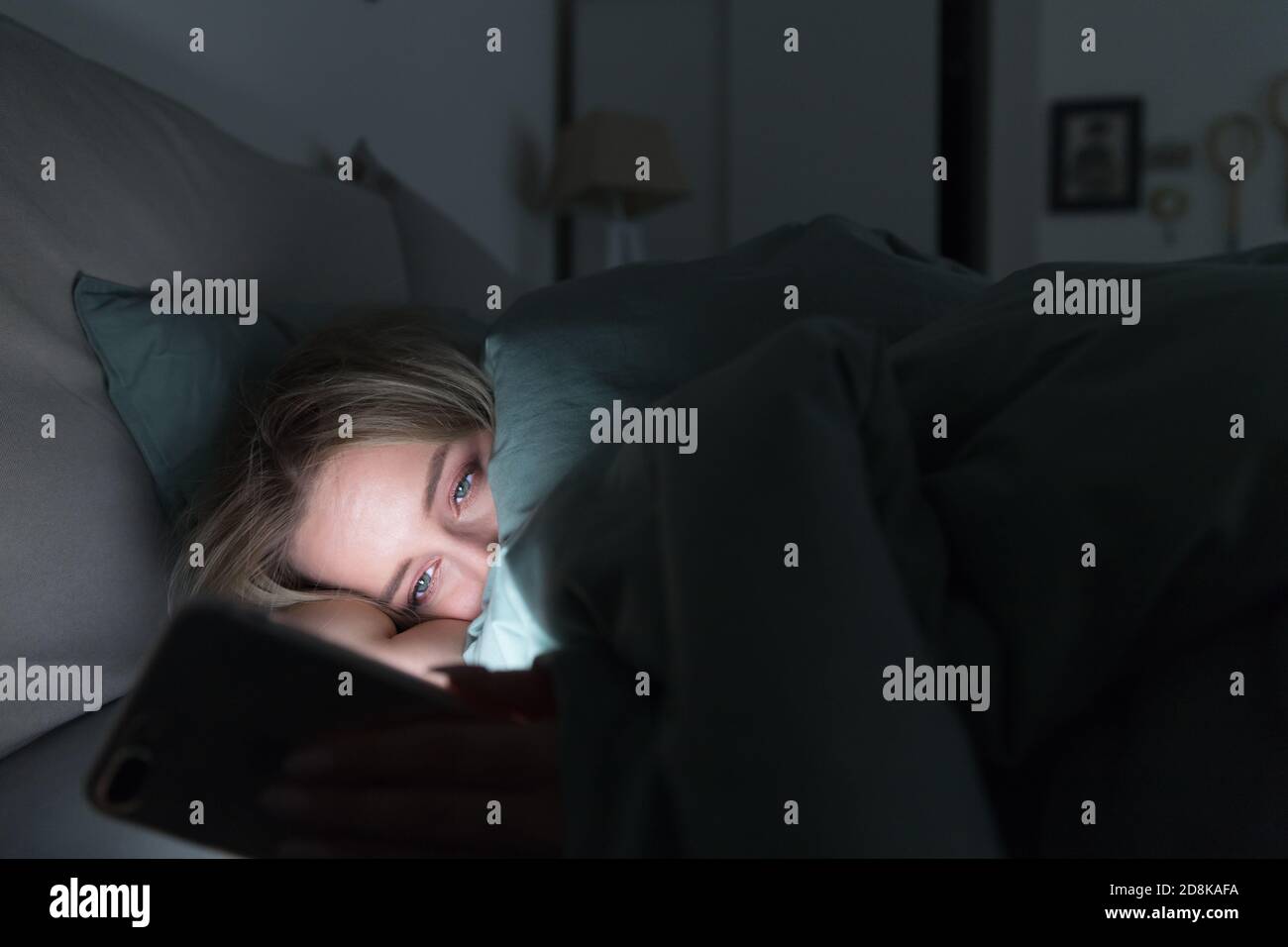 Sonnolenta donna stanca sdraiata a letto sotto la coperta utilizzando smartphone a tarda notte, non può dormire. Insonnia, nomofobia, disturbi del sonno concetto. Sociale Foto Stock