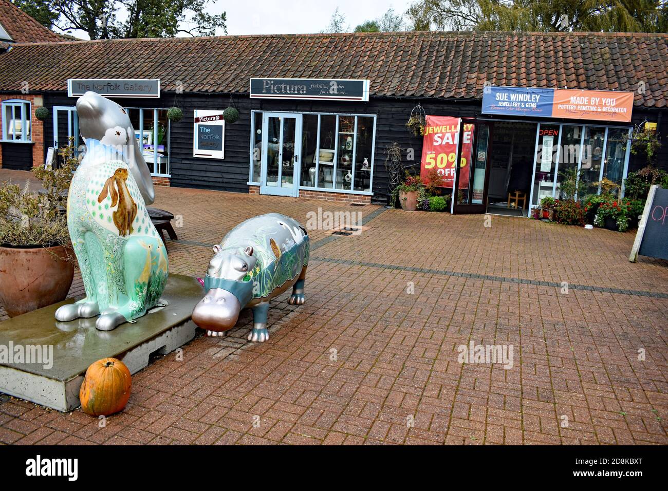 Sculture dipinte di coniglio e ippopotamo si trovano nel cortile di Wroxham Barns a Norfolk, Regno Unito. Negozi boutique e monolocali si trovano nel fienile. Foto Stock