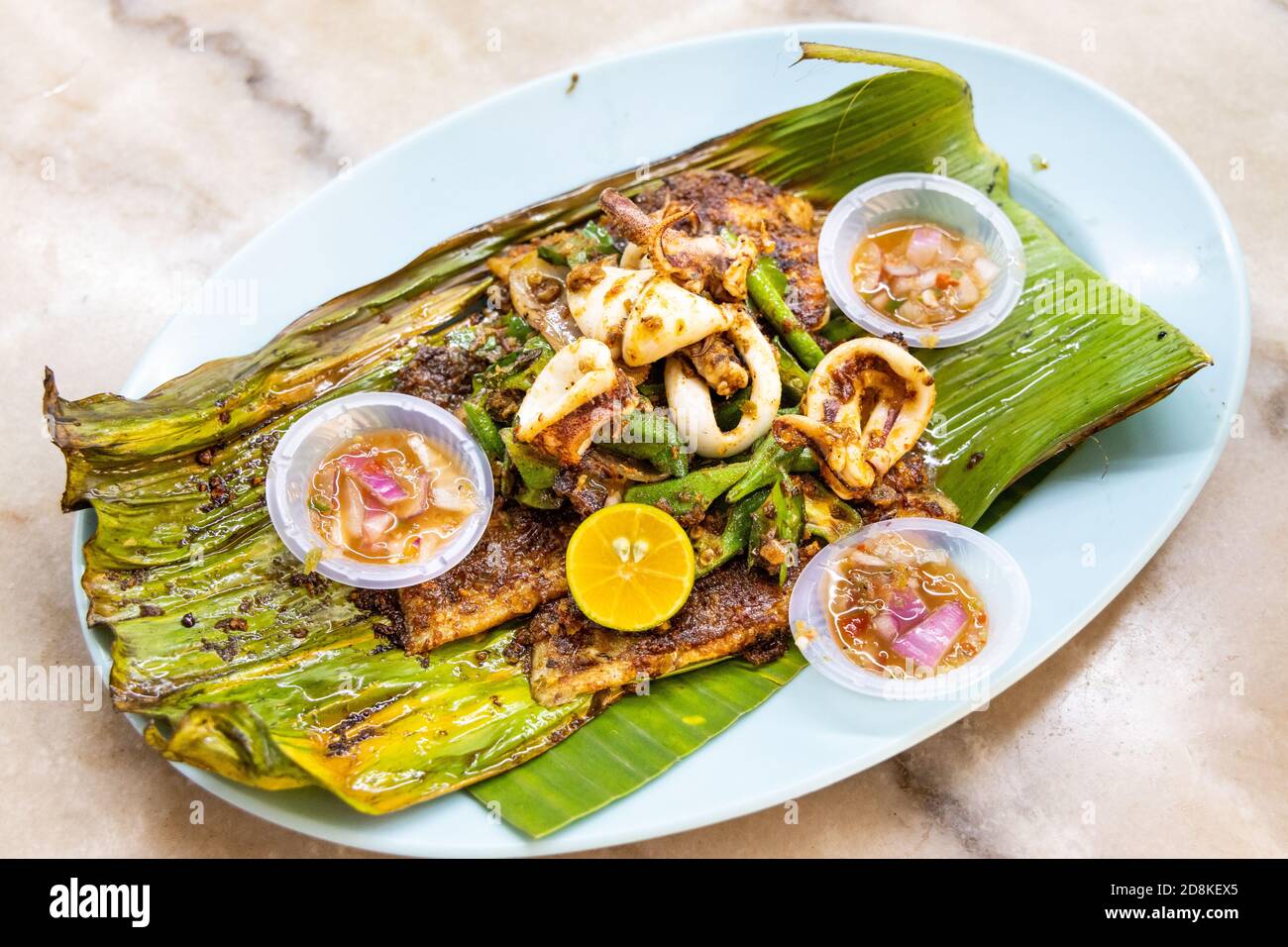 Filetto di pesce di stingray alla griglia con spezie su foglia di banana, popolare delicatezza della Malesia. Foto Stock