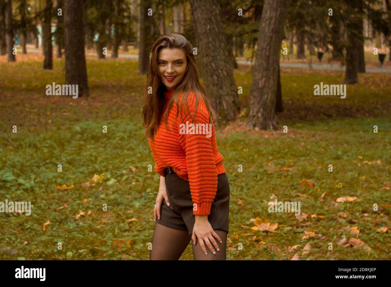 Brunette in autunno Parco e foglie d'autunno. Umore autunnale. Foglie gialle, rosse e verdi in un maglione rosso Foto Stock