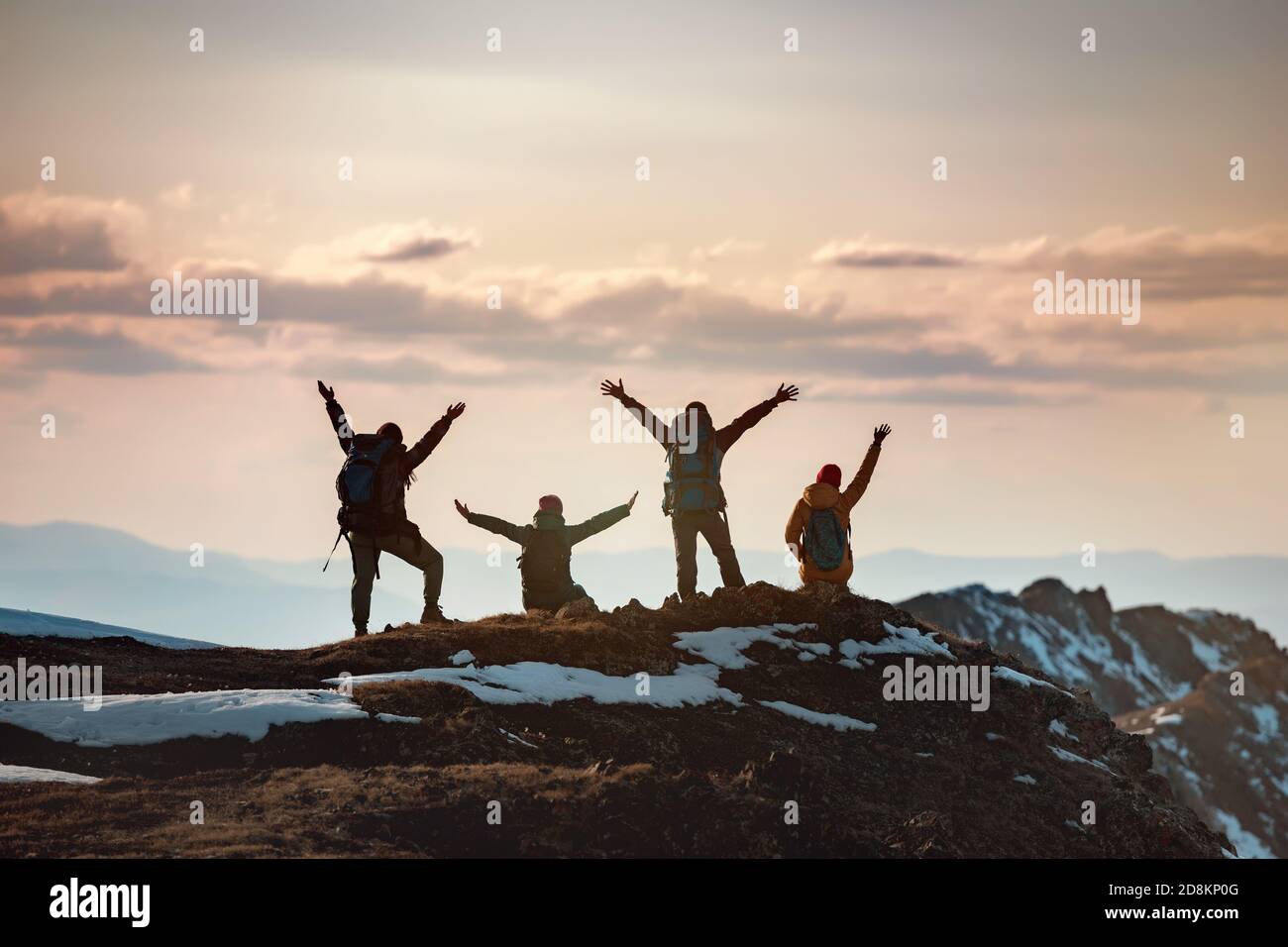 Gruppo di escursionisti felici si alza con le braccia sollevate in vincitore si posa in cima alla montagna e gode il tramonto Foto Stock