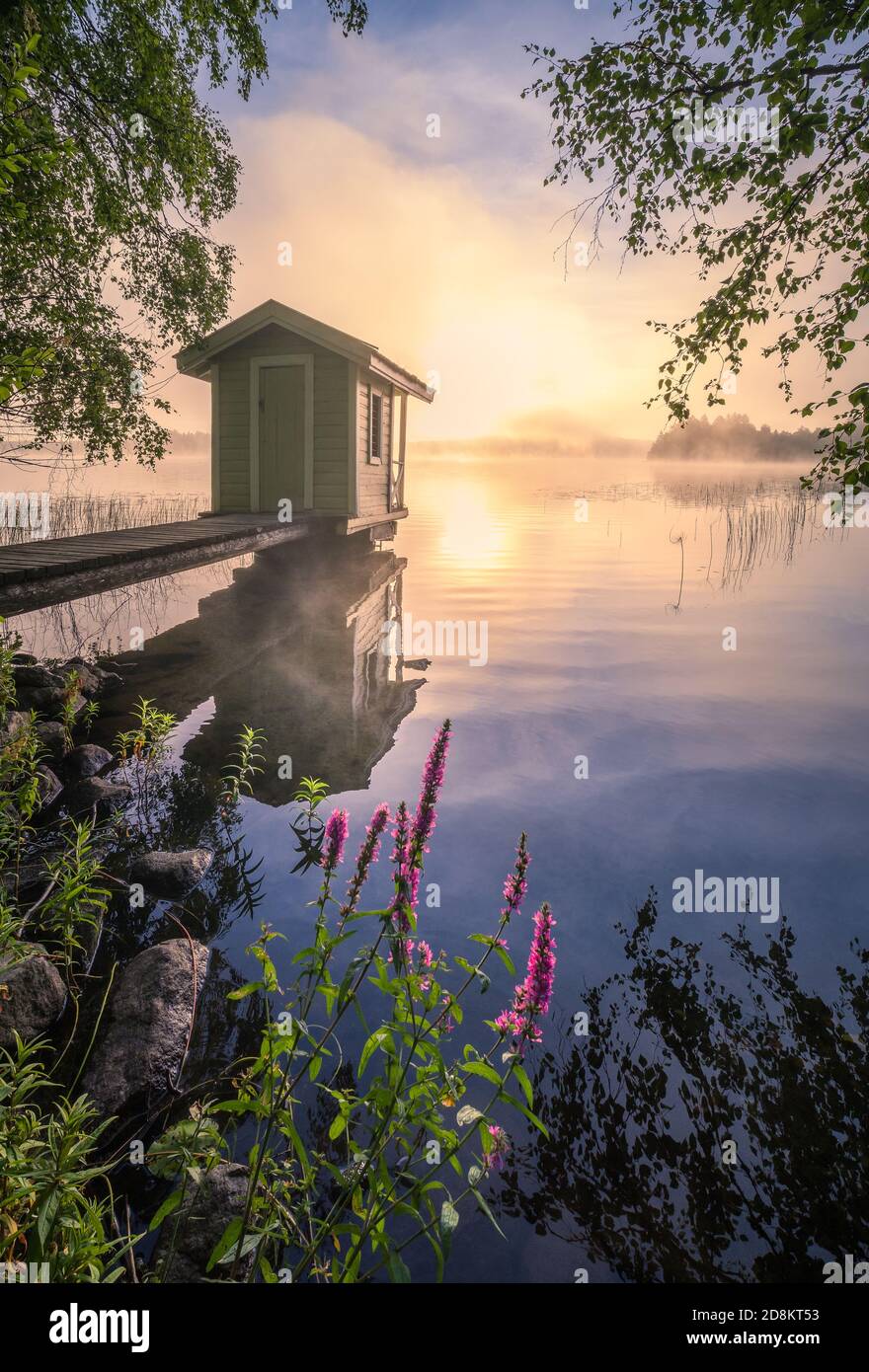 Splendido paesaggio mattutino con un piccolo cottage per nuotare, un molo e un'alba in riva al lago in Finlandia Foto Stock