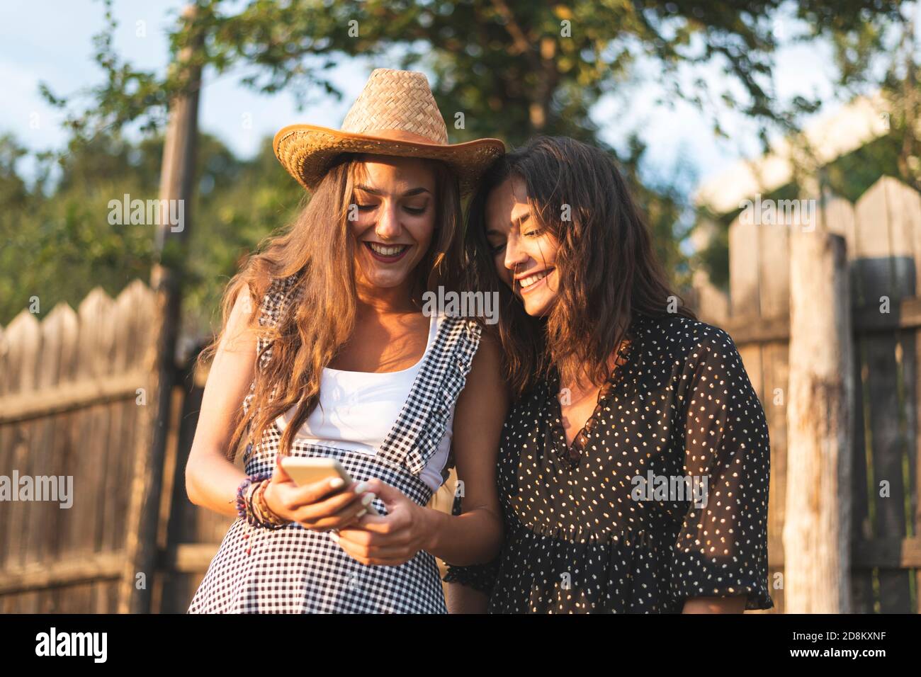 Due bellissime amiche che usano uno smartphone e sorridono. Ranch Concept Photography Foto Stock