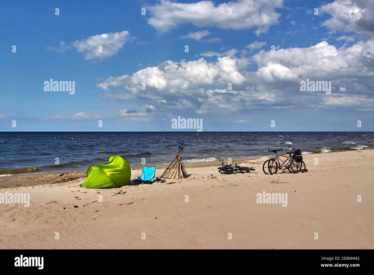 Biciclette parcheggiate su una spiaggia di mare presso la tenda verde e una sedia da spiaggia. Foto Stock
