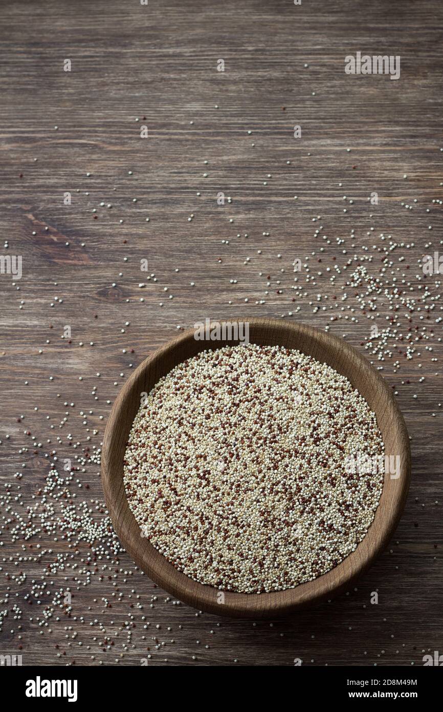 Quinoa crude mescolate in ciotola di legno su tavola di legno. Supercibo sano e senza glutine Foto Stock