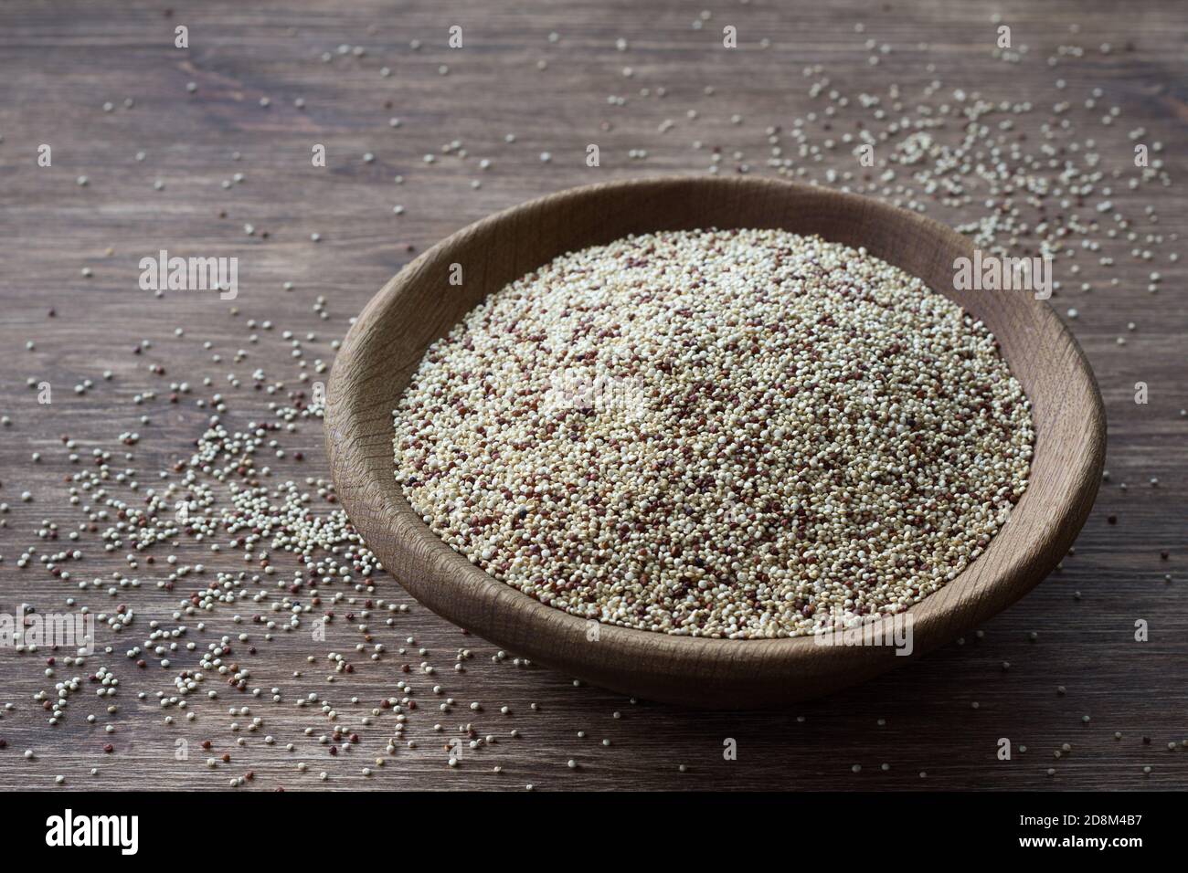 Quinoa crude mescolate in ciotola di legno su tavola di legno. Supercibo sano e senza glutine Foto Stock