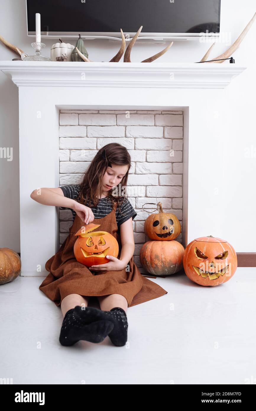 Bambina con zucca intagliata su Halloween a casa seduta accanto al camino in soggiorno. Trucco o trucco. Bambino che celebra Halloween Foto Stock
