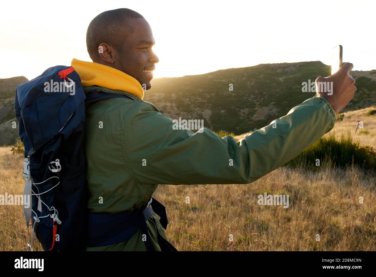 Profilo ritratto di felice afro-americano uomo con zaino prendendo selfie durante l'escursione in natura Foto Stock