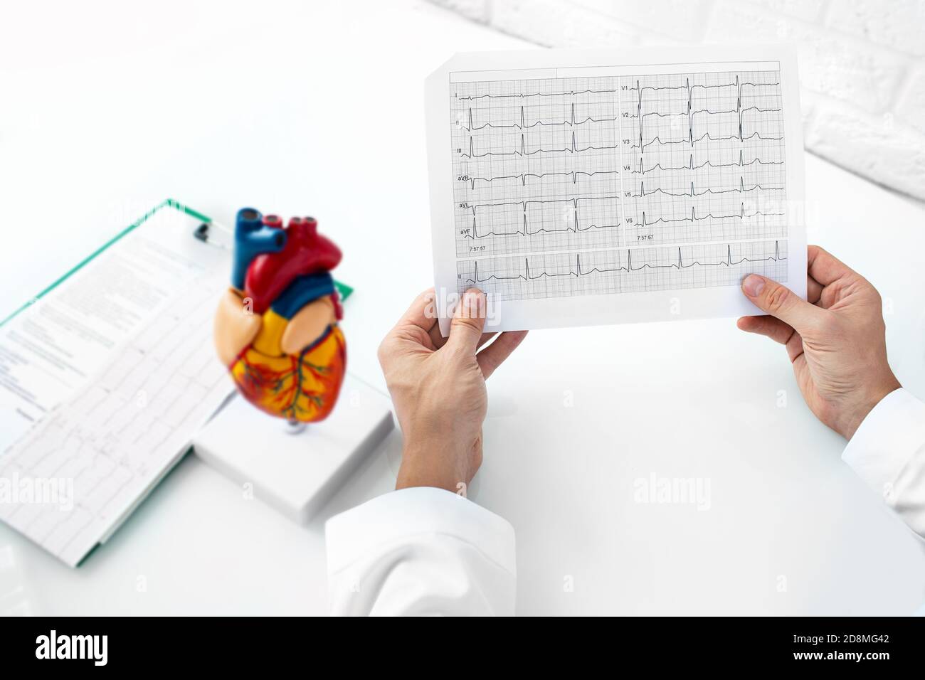 Cardiologo che analizza i risultati dell'elettrocardiogramma di un paziente nel suo ufficio medico. Malattie cardiache e cure mediche Foto Stock