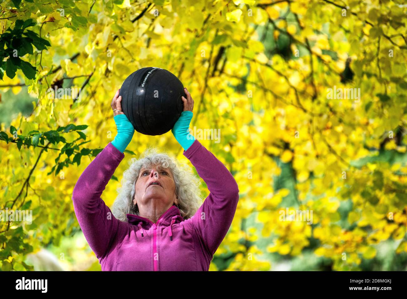 Una donna negli anni sessanta che solleva pesi all'aperto durante l'autunno. Foto Stock