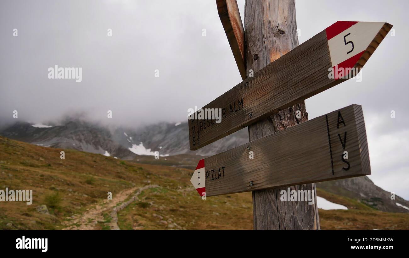 Vista in primo piano di cartelli in legno e segnavia che mostrano le indicazioni per Rescher Alm e Piz Lad in Alto Adige con montagne coperte di nubi. Foto Stock