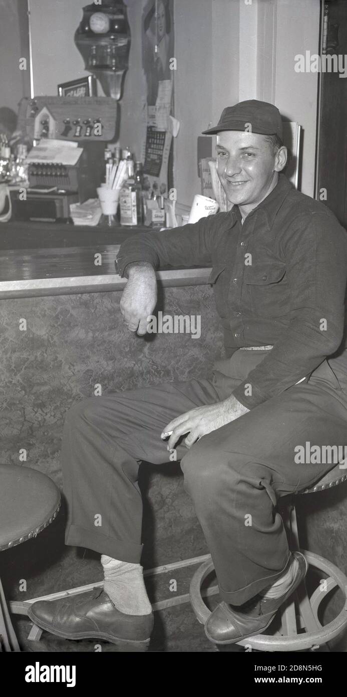Anni '50, storico, un lavoratore maschile rilassante dopo il lavoro seduto su uno sgabello su un bar, Eugene, Oregon, Stati Uniti. Foto Stock