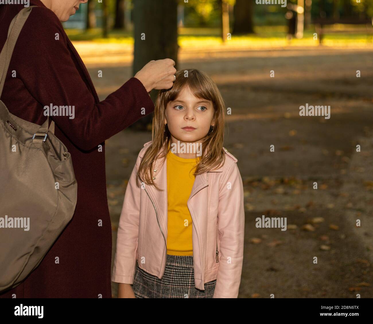 Le mani delle donne di una madre o di un caregiver fissano con cura una clip per capelli sui capelli di una bambina. Foto autunno all'aperto. Accessori per capelli. Felice Foto Stock