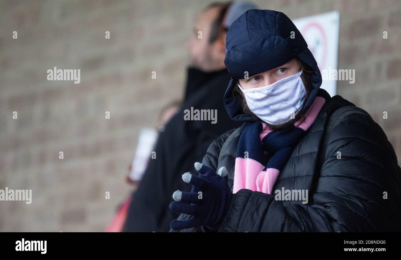 Un sostenitore del Dulwich Hamlet FC che indossa una sciarpa rosa e blu, un cappello, guanti e una maschera facciale durante una partita di calcio. Foto Stock