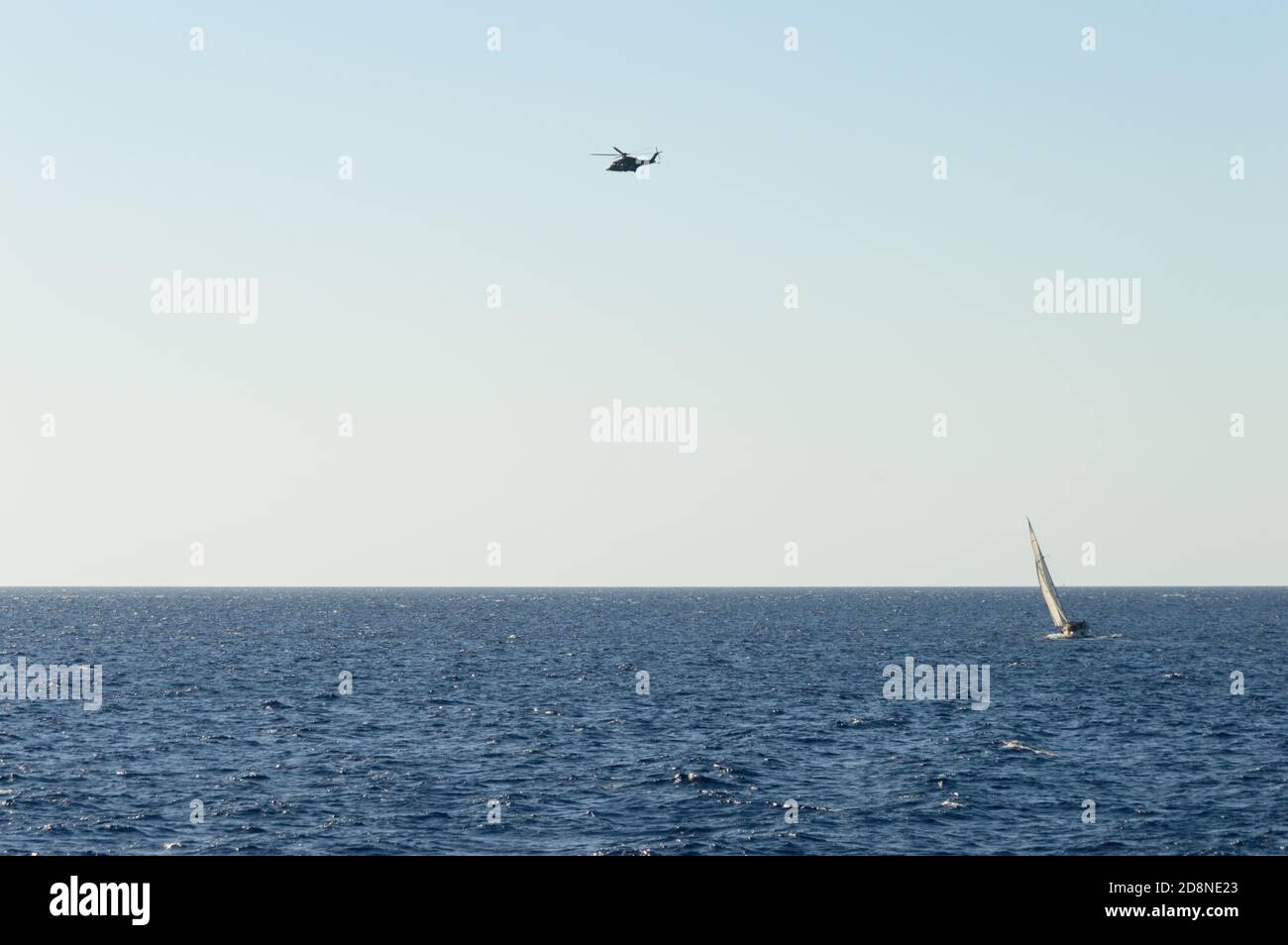 Una barca a vela e un elicottero in un'acqua blu orizzontale Foto Stock