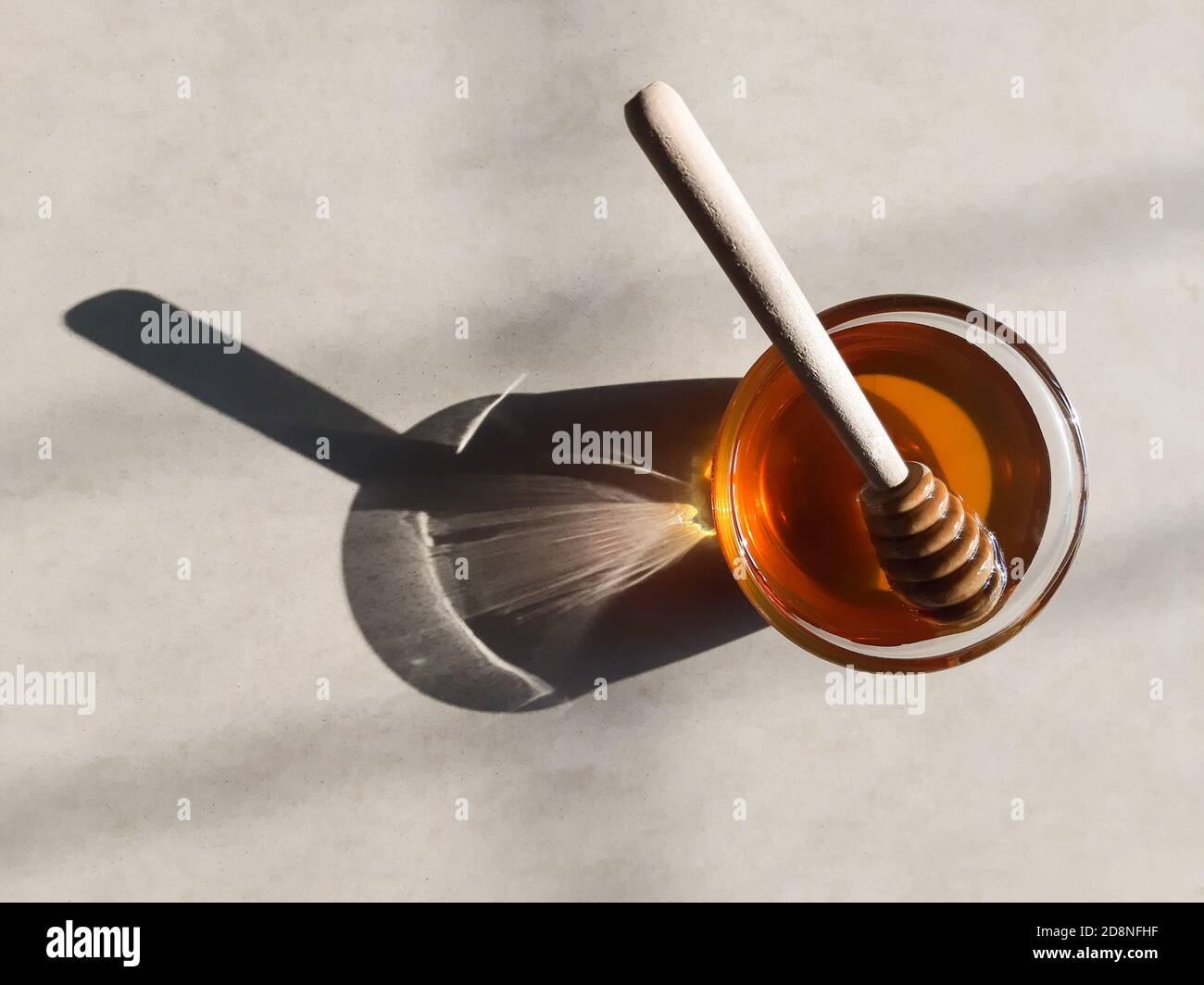 Cucchiaia di miele di legno in miele su fondo biancastro in miele naturale sunlight.fresh in recipiente di vetro con bastone di miele di legno. Foto Stock