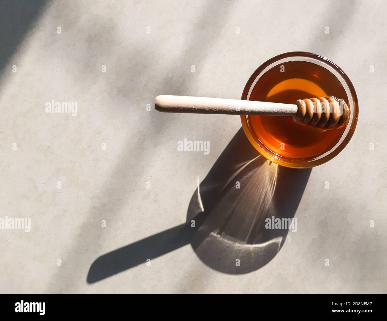 Cucchiaia di miele di legno in miele su fondo biancastro in miele naturale sunlight.fresh in recipiente di vetro con bastone di miele di legno. Foto Stock