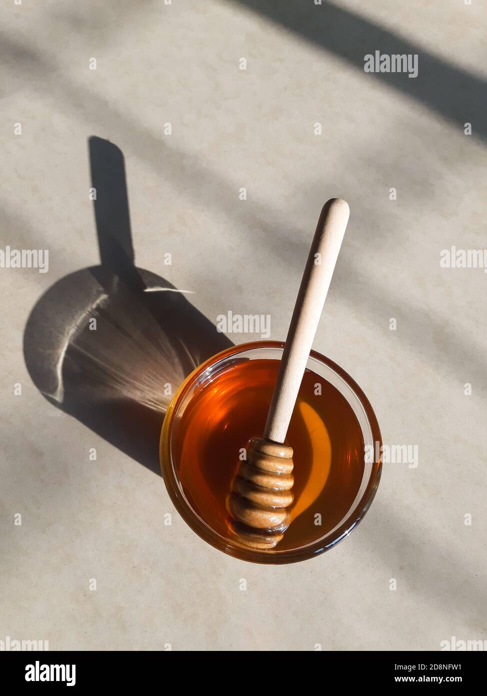 Cucchiaia di miele di legno in miele su fondo biancastro in miele naturale sunlight.fresh in recipiente di vetro con bastone di miele di legno. Foto Stock