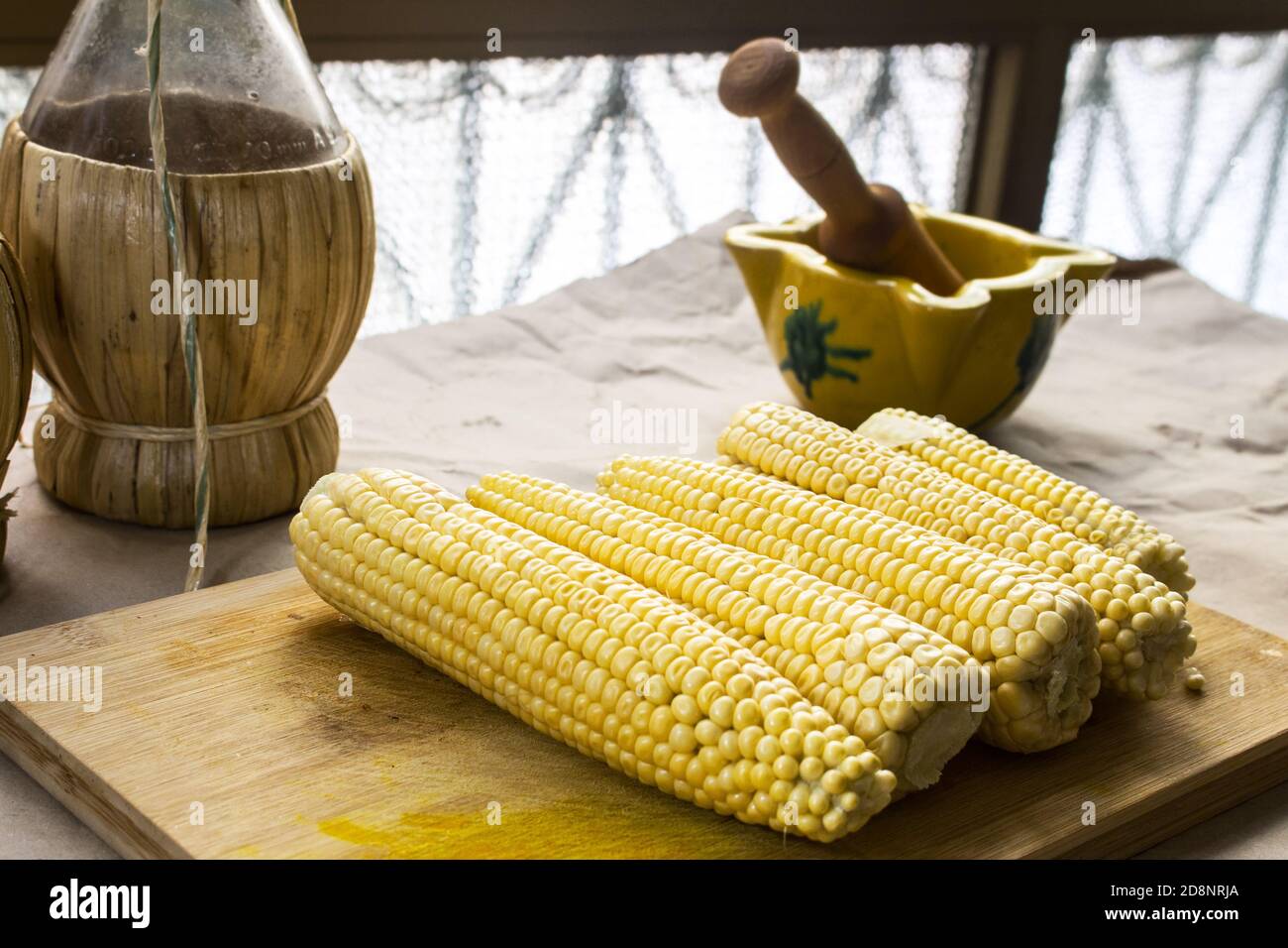 Granoturco crudo su un tagliere di legno, sullo sfondo un mortaio di ceramica valenciana e un vaso di vimini Foto Stock