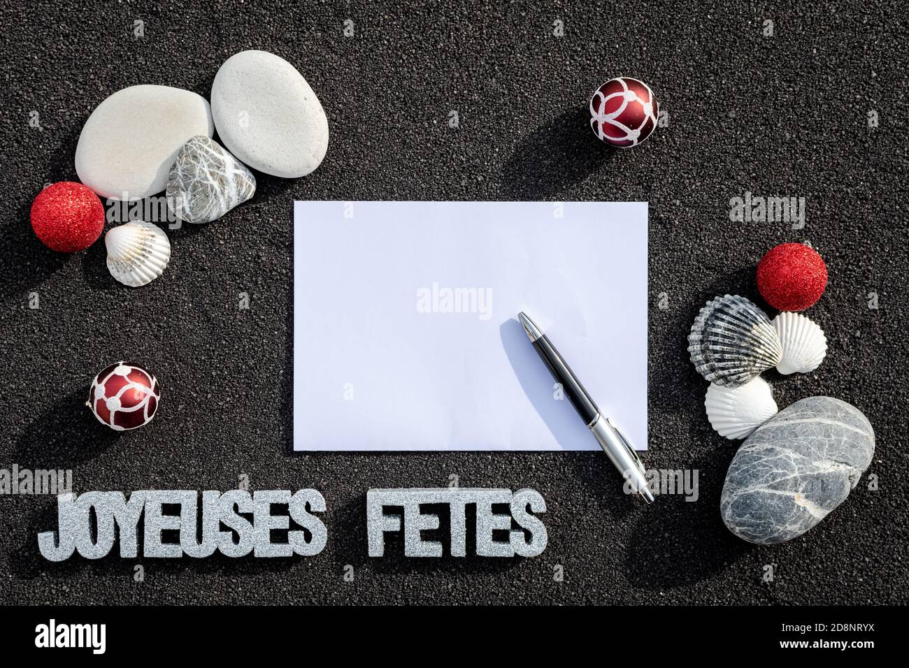 Arrière-plan grains de sable de mer, sable fin noir de plage avec envelope et galets. Emplacement pour texte sur papier. Galets en forme de petit pie Foto Stock