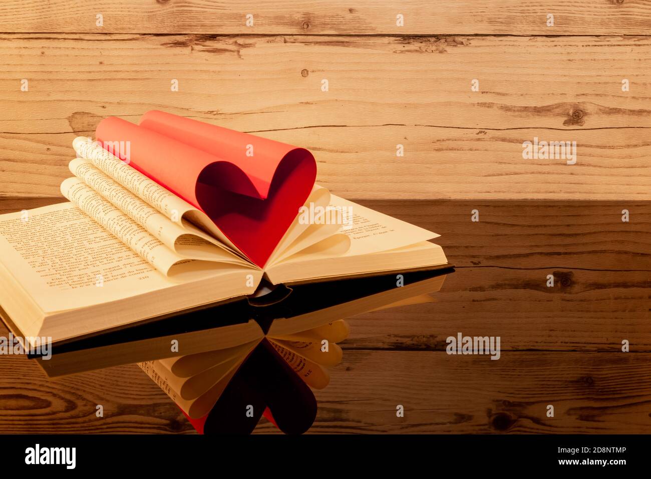 Libro ripiegato a forma di cuore su sfondo ligneo con riflessi. Foto Stock