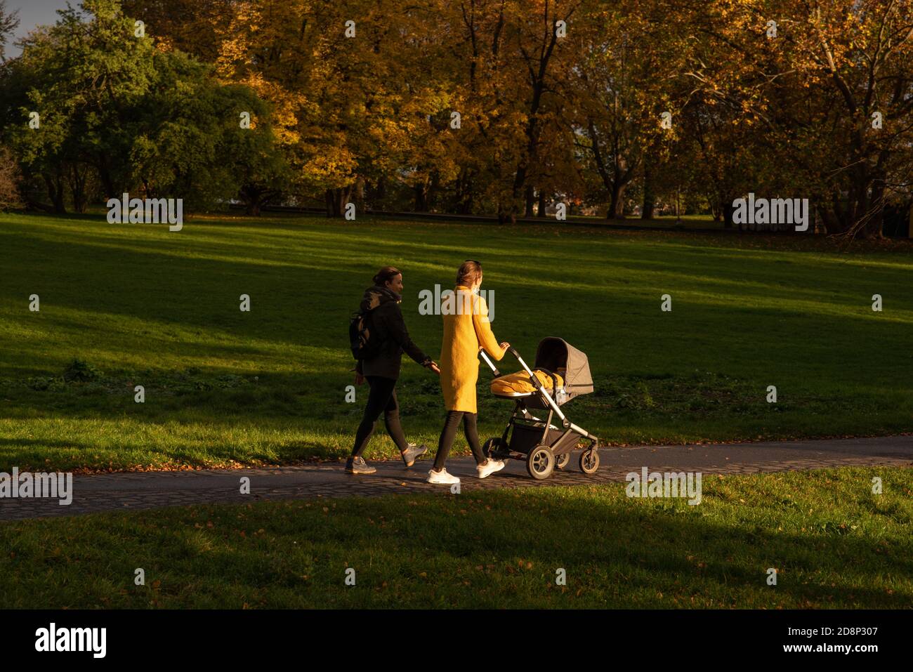 Due amici camminano sul parco mentre uno sta portando un passeggino con un bambino a Praga, repubblica Ceca Foto Stock