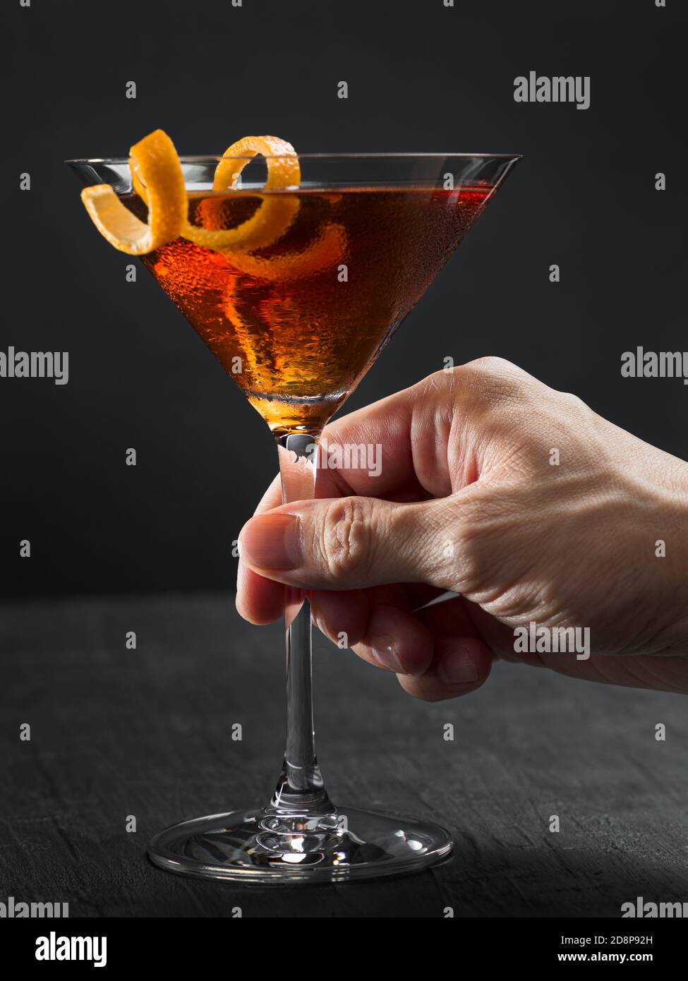 Mano dell'uomo che tiene un bicchiere da cocktail con un tocco arancione.  Preparazione di Manhattan Foto stock - Alamy