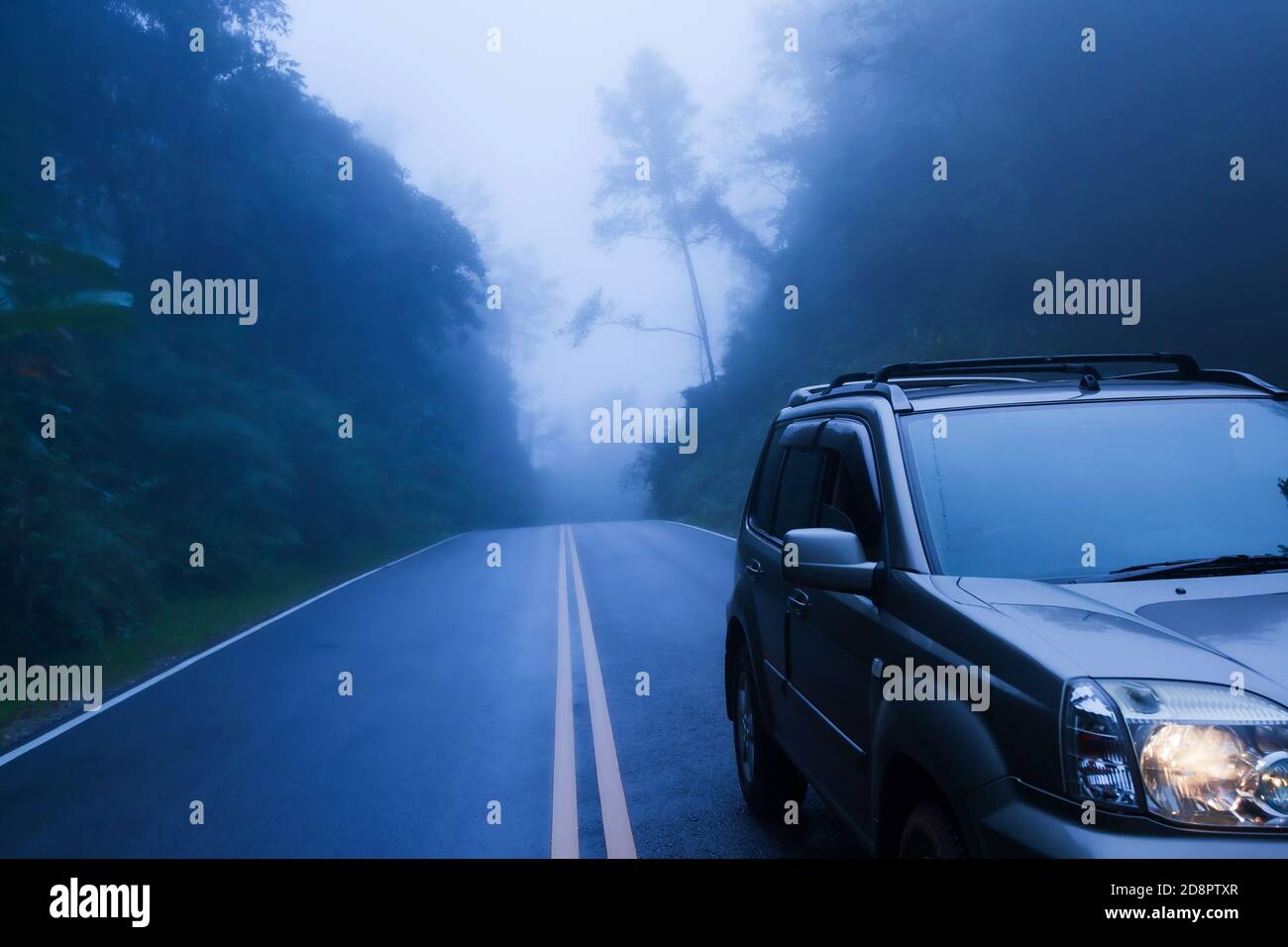 Vista frontale dell'auto SUV color argento su una strada di montagna, parcheggio SUV argento sul lato della strada nella nebbia blu. Messa a fuoco selettiva. Foto Stock