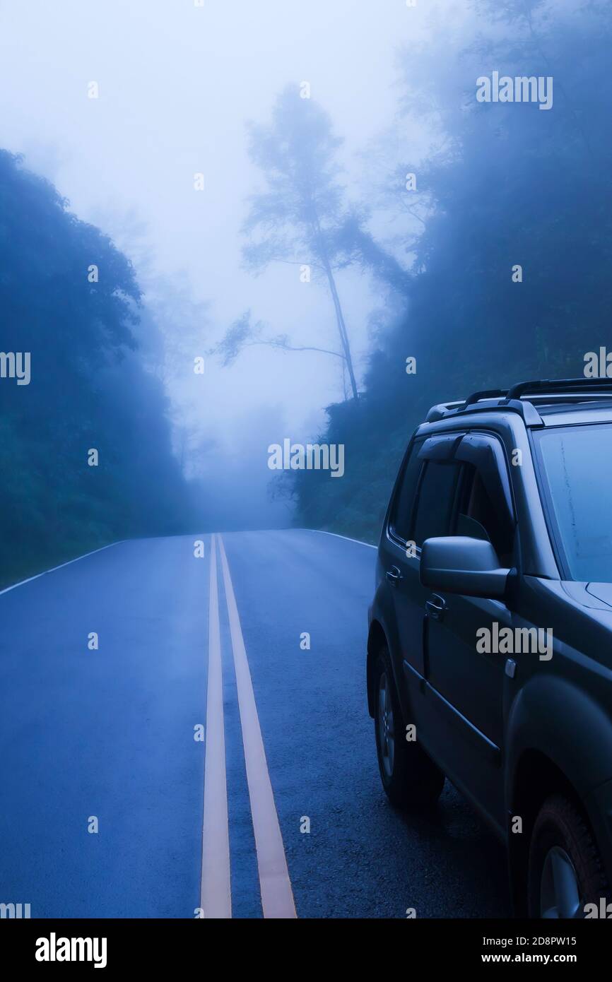 Vista frontale dell'auto SUV color argento su una strada di montagna, parcheggio SUV argento sul lato della strada nella nebbia blu. Messa a fuoco selettiva. Foto Stock