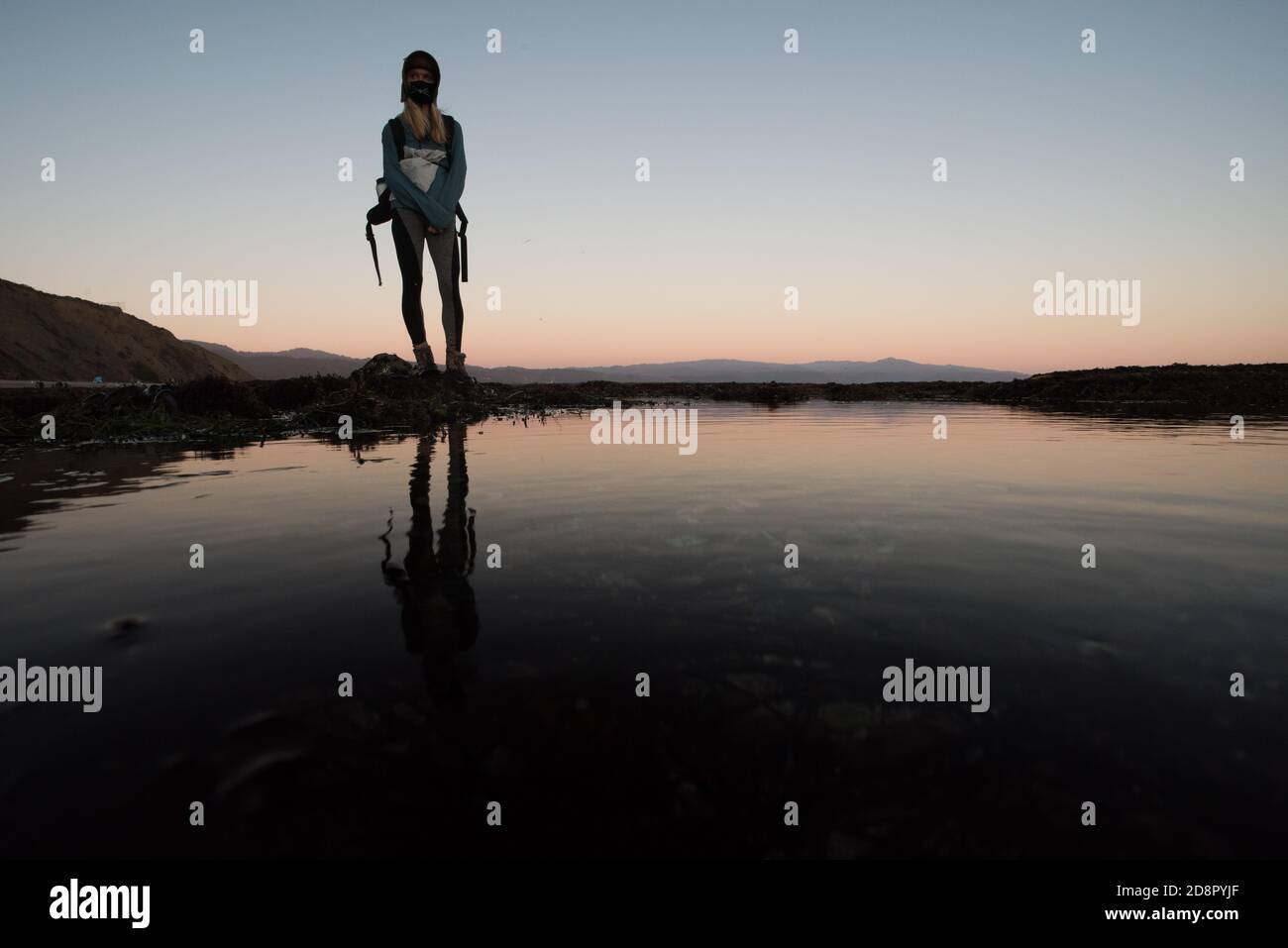Una donna che si trova sopra le piscine di marea del punto della colonna in California in tarda serata mentre il sole tramonta. Foto Stock