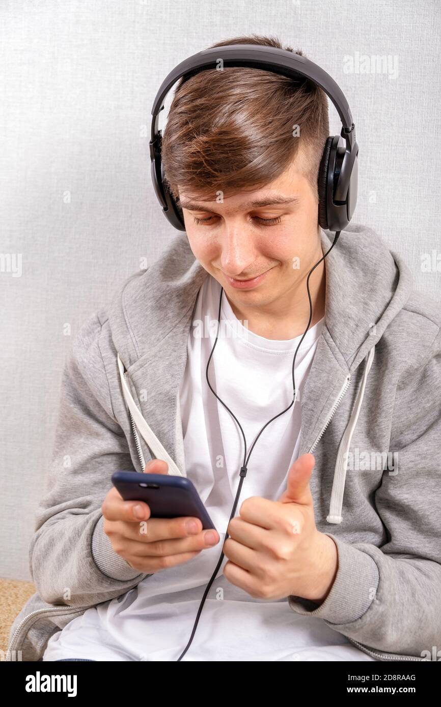 Il giovane uomo in cuffia usa un telefono sul bianco Sfondo parete Foto Stock