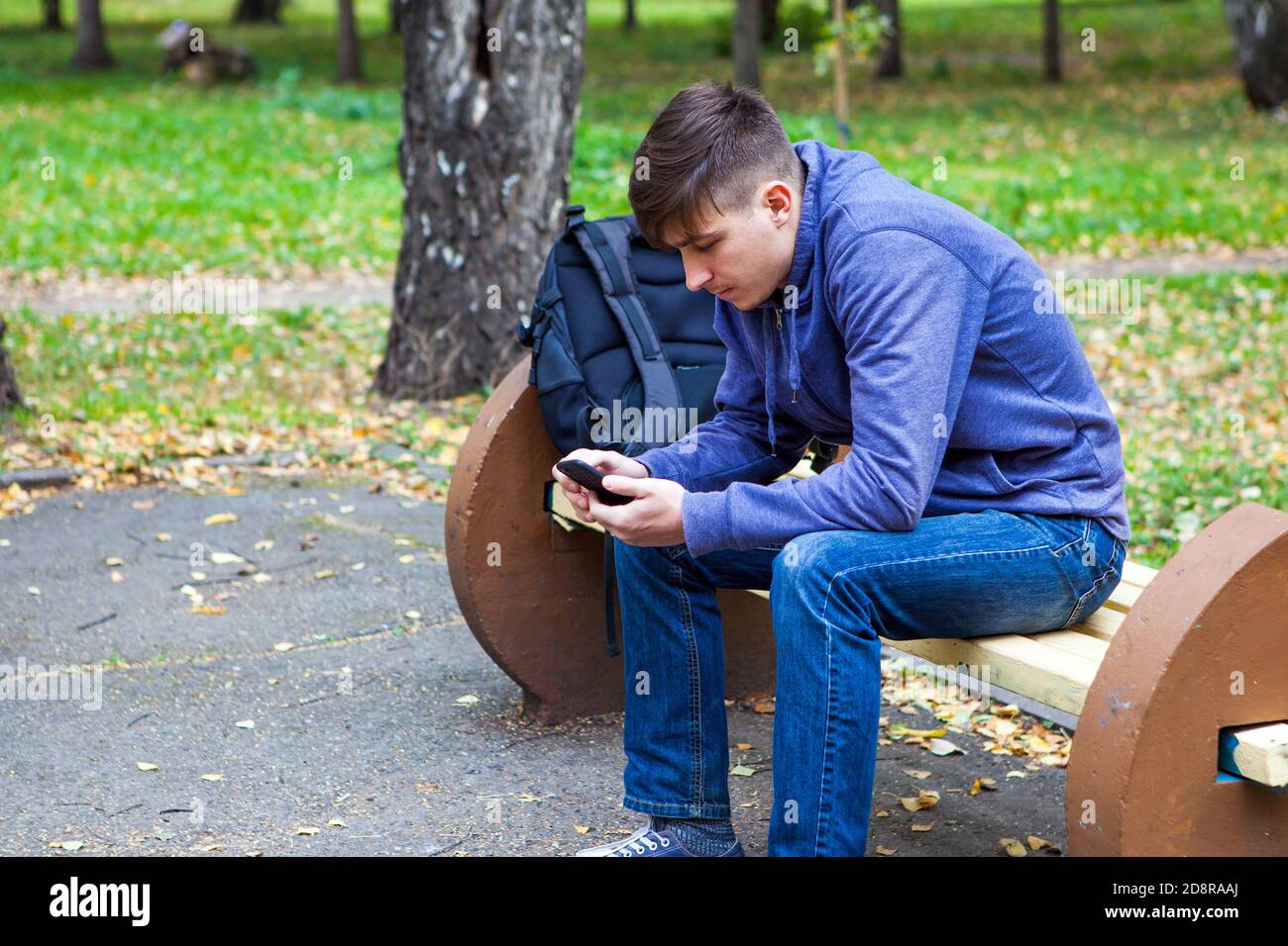 L'uomo giovane pensivo con un telefono siediti sul banco Nel Parco Autunno Foto Stock