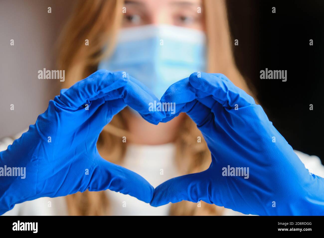 Colpo orizzontale di un simbolo del cuore formato dalla mano del medico in guanti blu di protezione. Foto Stock