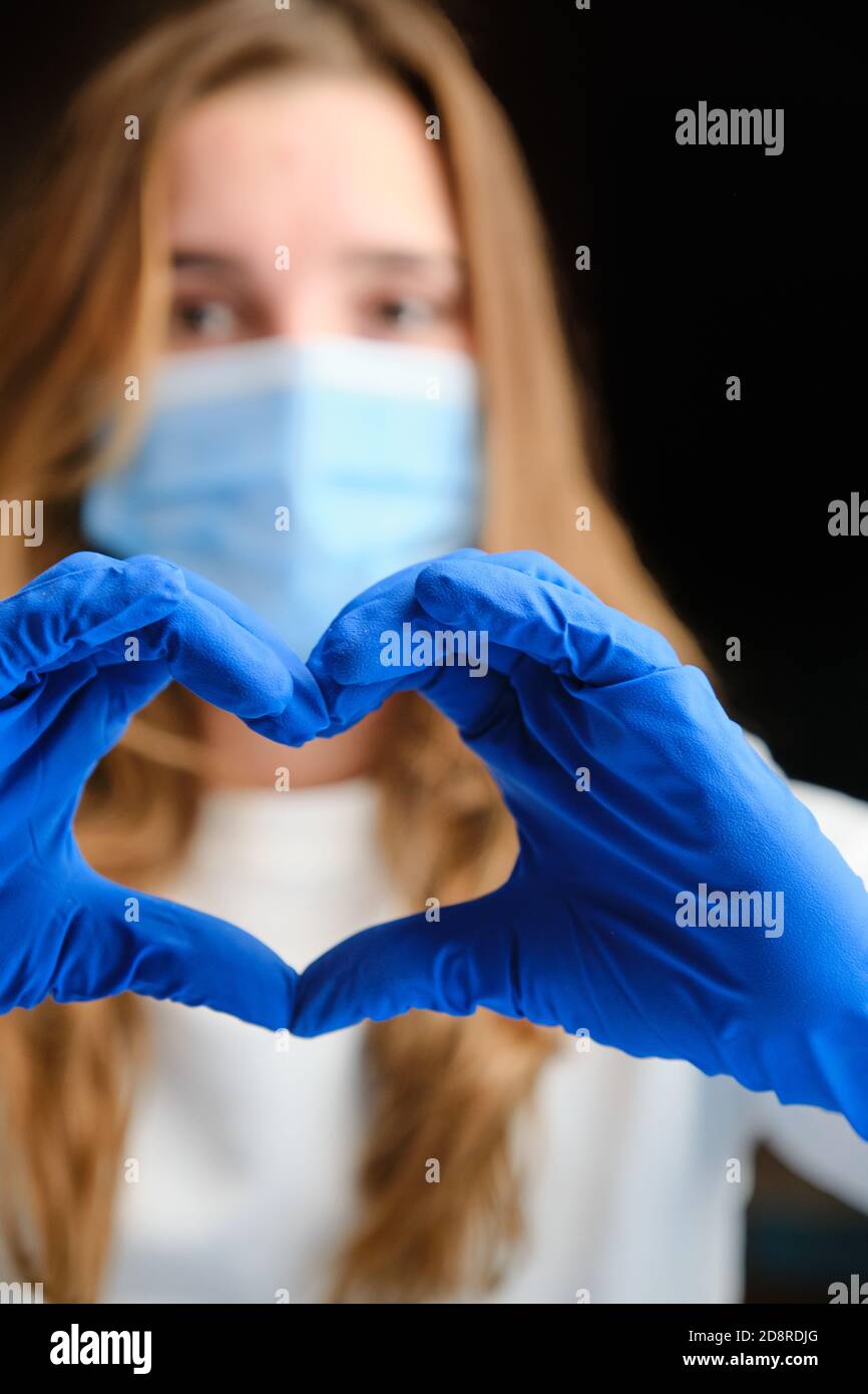 Colpo verticale di un simbolo del cuore formato dalla mano del medico in guanti blu di protezione. Foto Stock