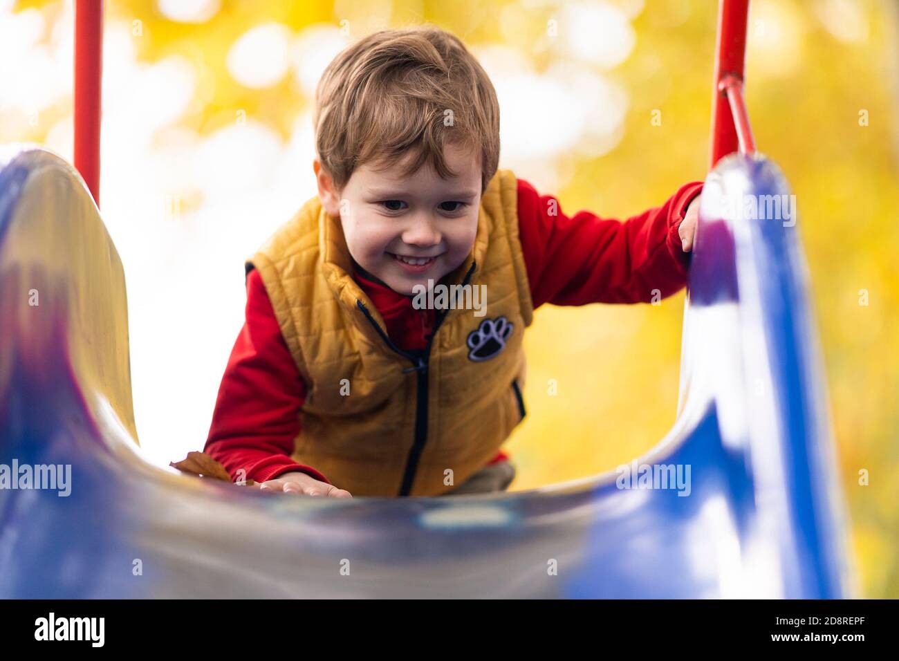 Felice bambino sorridente che sale su una cornice / scivolo in un parco giochi all'aperto. Foto Stock