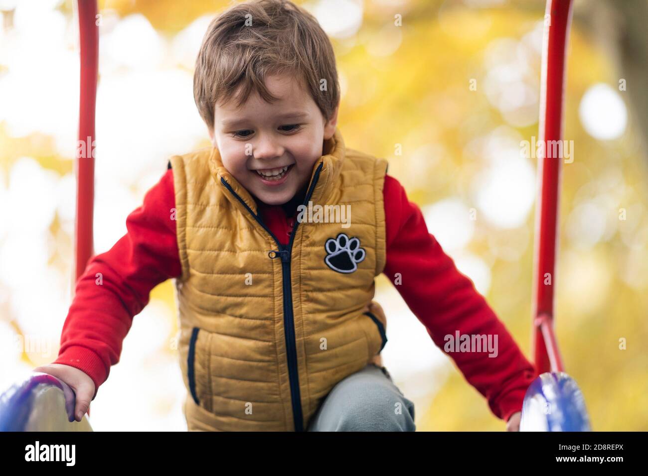 Felice bambino sorridente che sale su una cornice / scivolo in un parco giochi all'aperto. Foto Stock