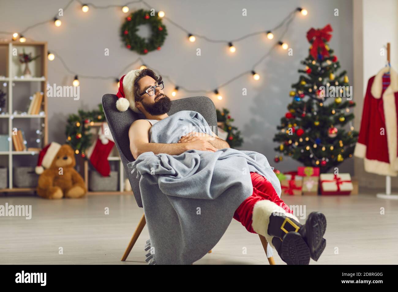 Giovane stanco vestito da Babbo Natale che dorme in pace una comoda  poltrona sotto una calda coperta Foto stock - Alamy