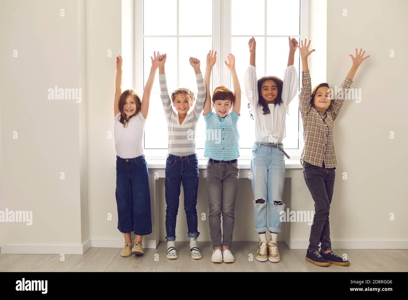 Gruppo di bambini diversi di compagni di classe si levano in piedi con le mani sollevate nel corridoio della scuola. Foto Stock