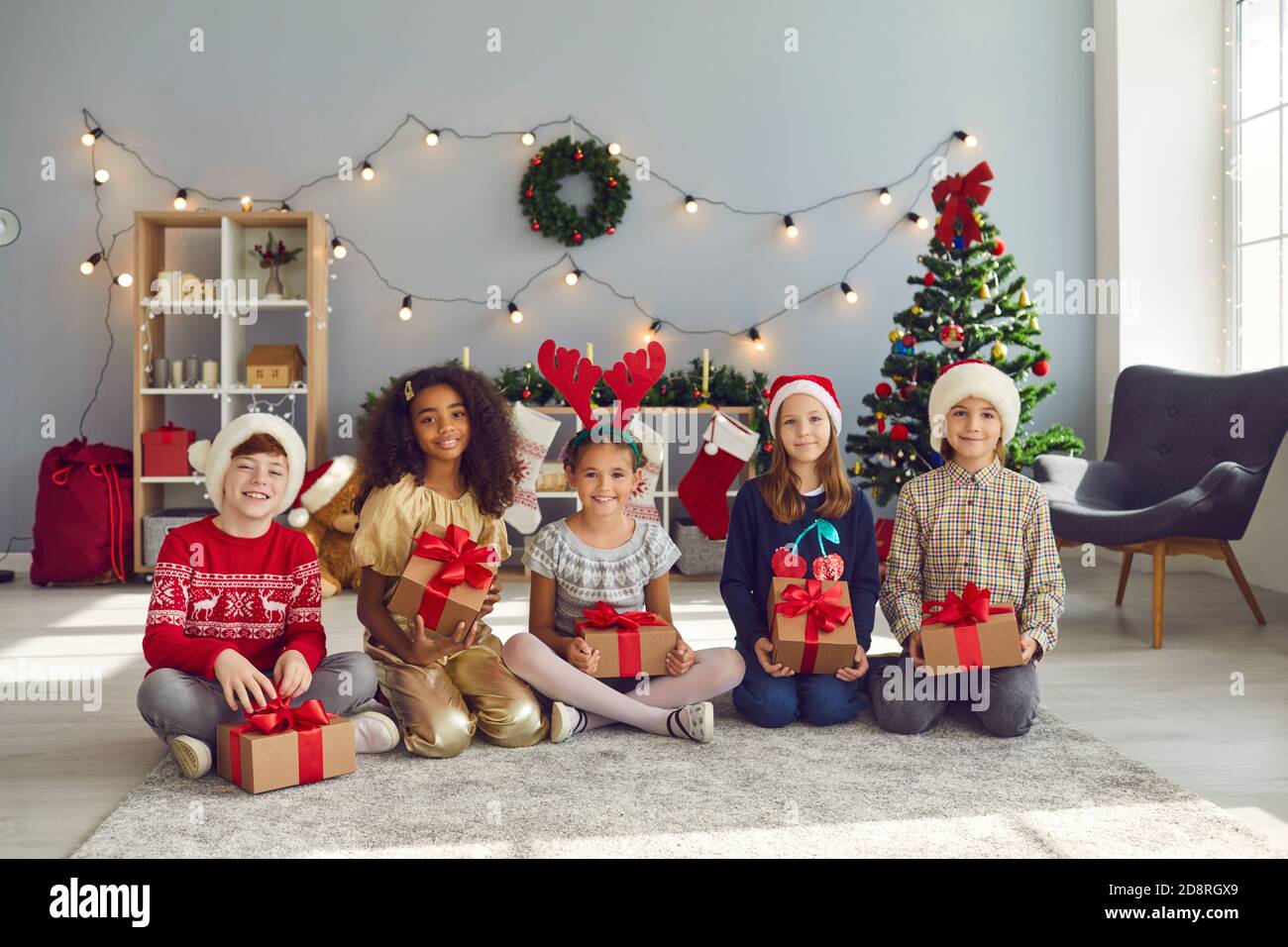 Felici i bambini seduti sul pavimento a casa, tenendo i loro regali di Natale e guardando la macchina fotografica Foto Stock