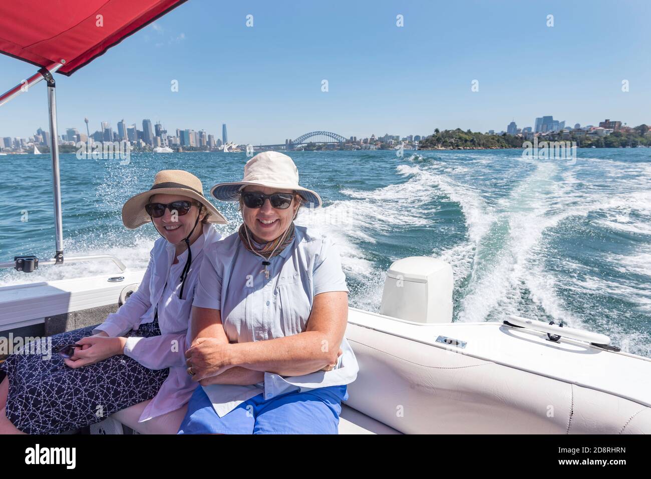 Due donne australiane di mezza età che cavalcano in un motoscafo sul porto di Sydney, indossando cappelli e protezione solare Foto Stock